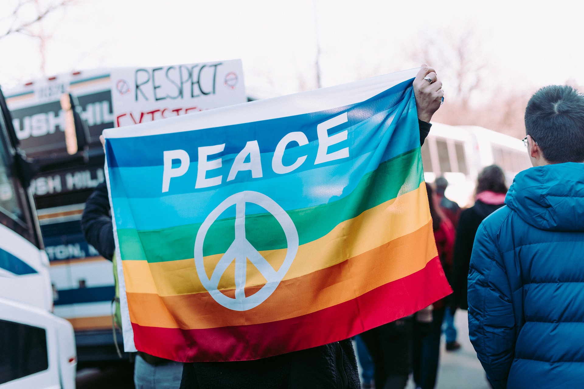 Person holding a rainbow flag with the word peace written on it at a larger gathering